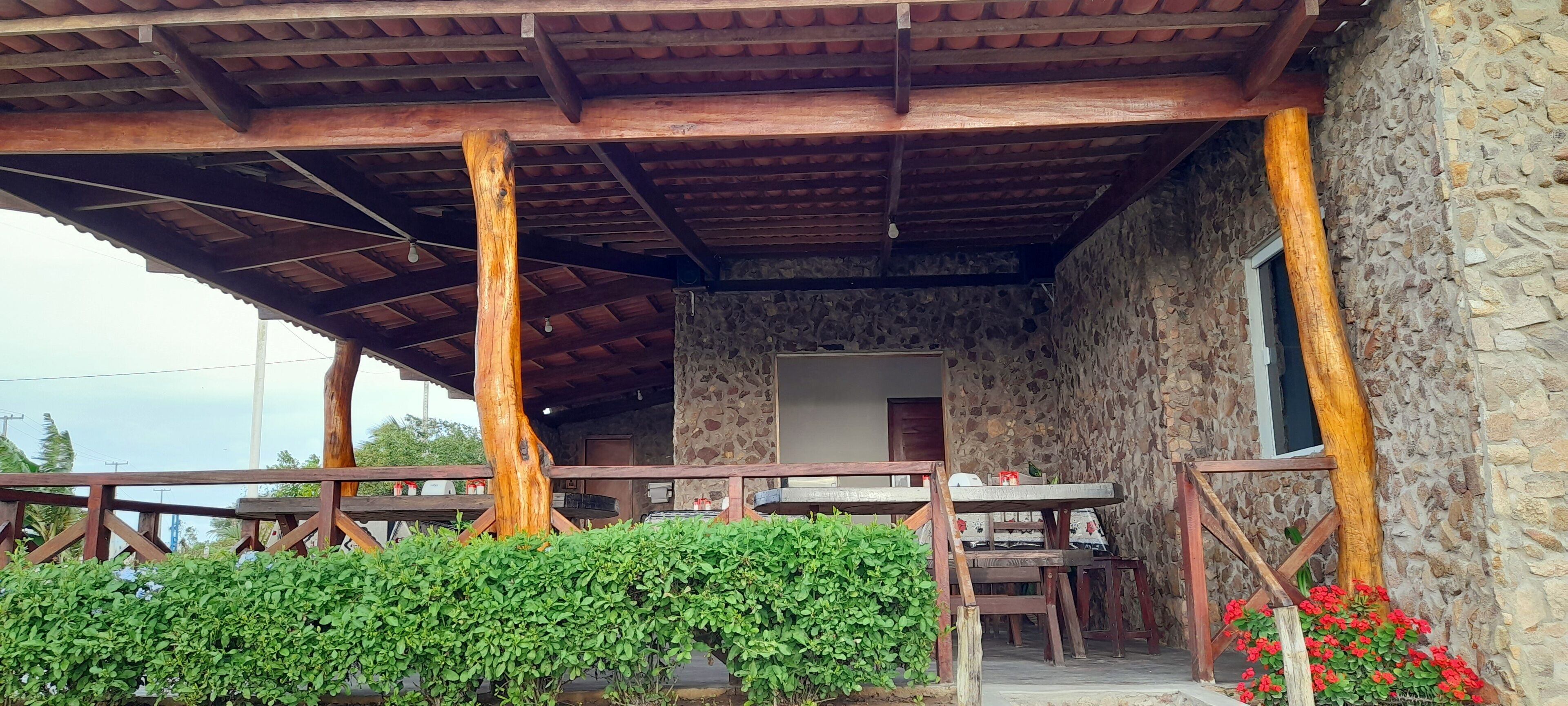 A rustic outdoor seating area with wooden tables and chairs, a stone wall, and a wooden pergola.