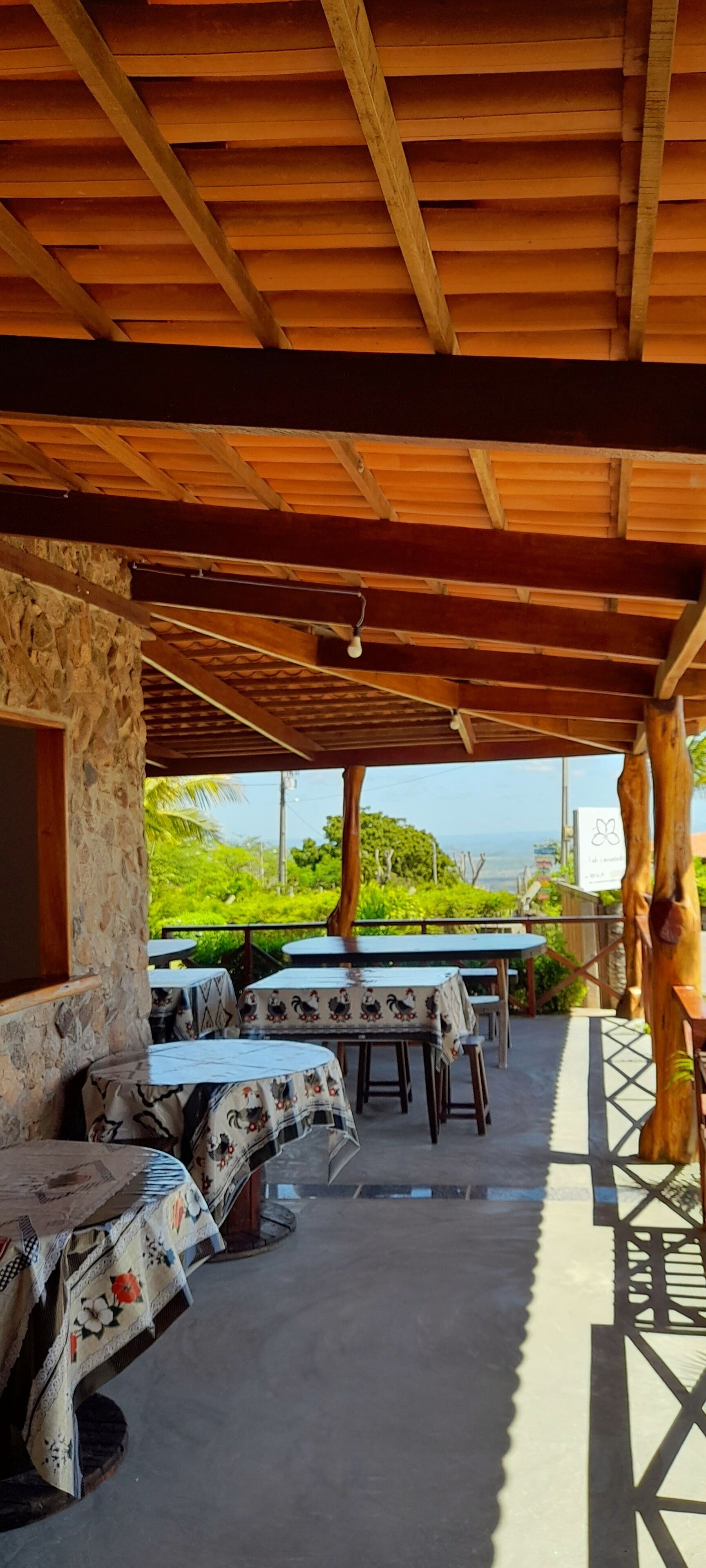 An outdoor patio with wooden tables and benches, stone walls, and a view of the ocean.
