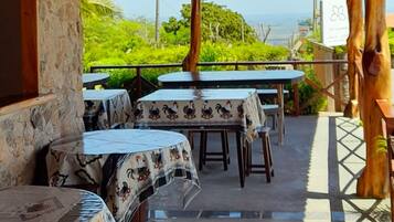 An outdoor patio with wooden tables and benches, stone walls, and a view of the ocean.