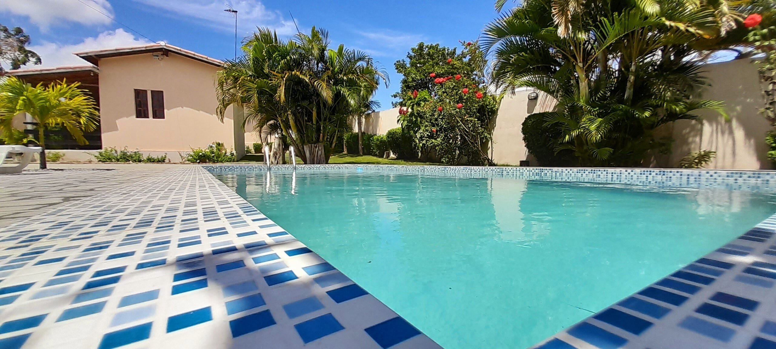 A swimming pool with a tiled edge, surrounded by palm trees and a building with a beige facade.