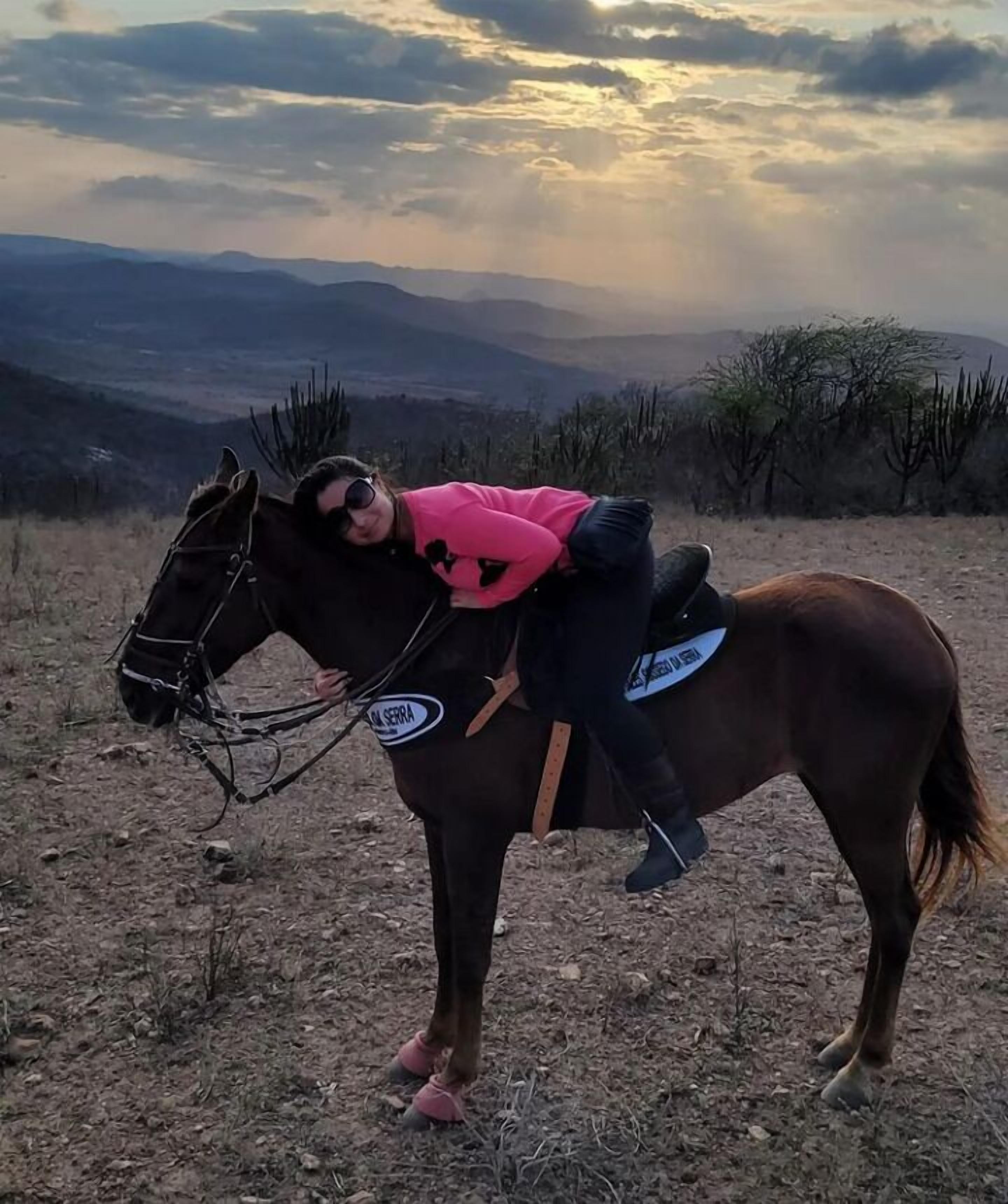 A person riding a horse on a dry, rocky terrain with sparse vegetation and distant mountains under a cloudy sky.