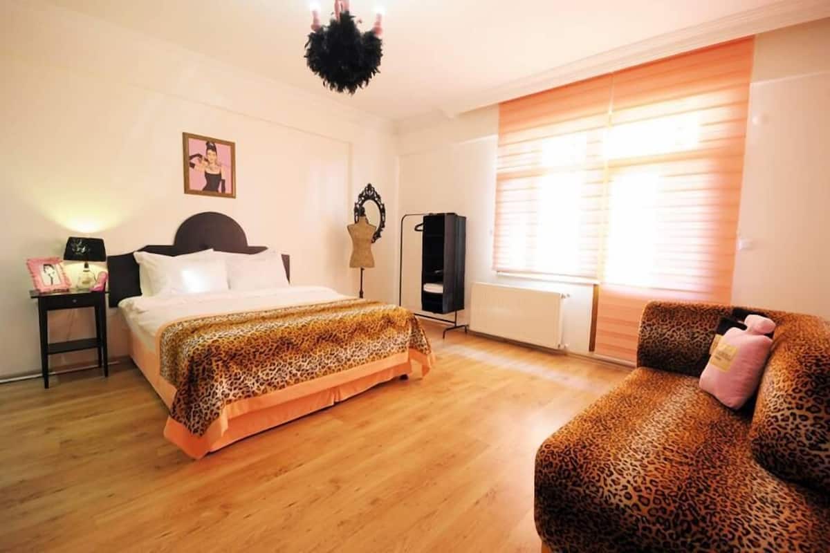 Une chambre à coucher avec un lit, un canapé à motifs léopard, un radiateur et une fenêtre avec des stores.