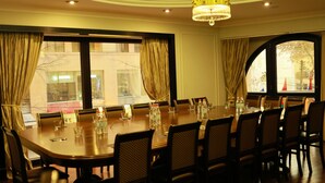 Un salón de conferencias con una mesa redonda, sillas, una araña y ventanas amplias con cortinas.
