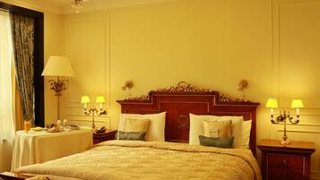 A spacious bedroom with a large bed, a wooden bench, a chandelier, and two bedside tables with lamps.