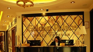 Un mostrador de recepción en el Hotel Golden Palace con diseño de mármol, una araña y un recepcionista.