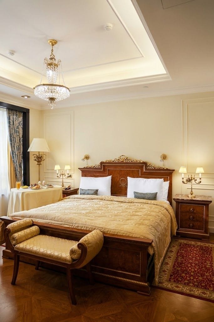 Ein Hotelzimmer mit einem großen Bett, einem Holz-Kopfteil, Nachttischen mit Lampen, einer Bank und einer Kandelaber.