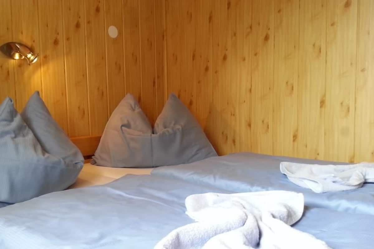 Quarto com paredes de madeira, uma cama com roupa de cama azul e duas almofadas.