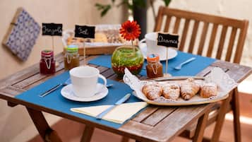 A wooden table with a blue placemat, a white cup, a plate of pastries, and various jars of jam and honey.