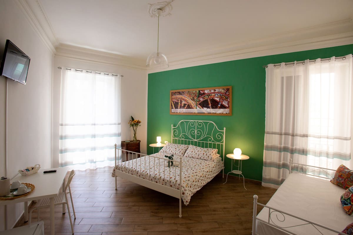 A bedroom with a bed, a desk, a chair, a television, and a green wall.