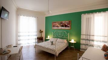 A bedroom with a bed, a desk, a chair, a television, and a green wall.