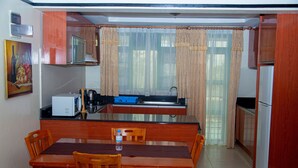 A compact kitchen with wooden cabinets, a dining table, and chairs. - Highlands Suites Hotel (Kigali)