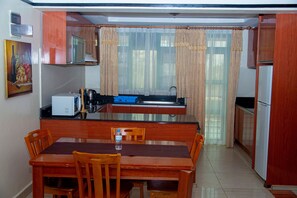 A compact kitchen with wooden cabinets, a dining table, and chairs. - Highlands Suites Hotel (Kigali)