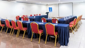 A conference room with multiple tables, red and gold chairs, and a projector screen. - Highlands Suites Hotel (Kigali)
