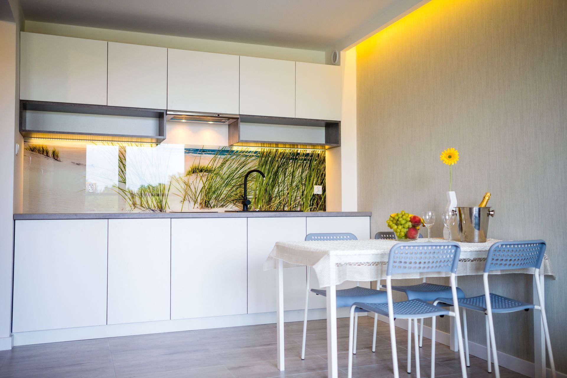 Une cuisine moderne avec des armoires blanches, un barbecue intégré et un revêtement mural décoré de plantes vertes.