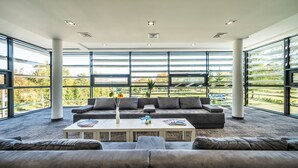 A modern living room with a large gray sectional sofa, a white coffee table, and a view of a park through large windows. - Apart Hotel Residence Jastrzębia Góra (Wladyslawowo)
