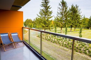 Varanda com duas cadeiras de descanso, vista de um jardim ajardinado com árvores e um espaço pavimentado.