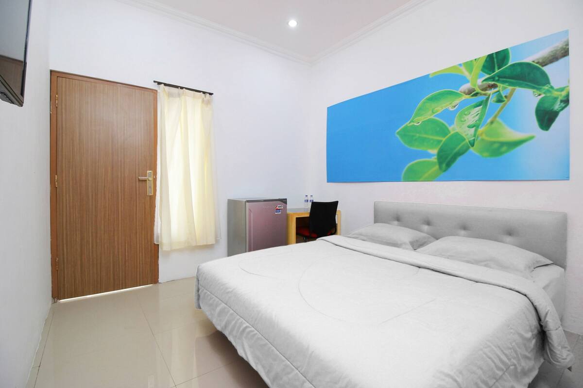 A bedroom with a bed, a desk, a chair, a wardrobe, and a painting on the wall.