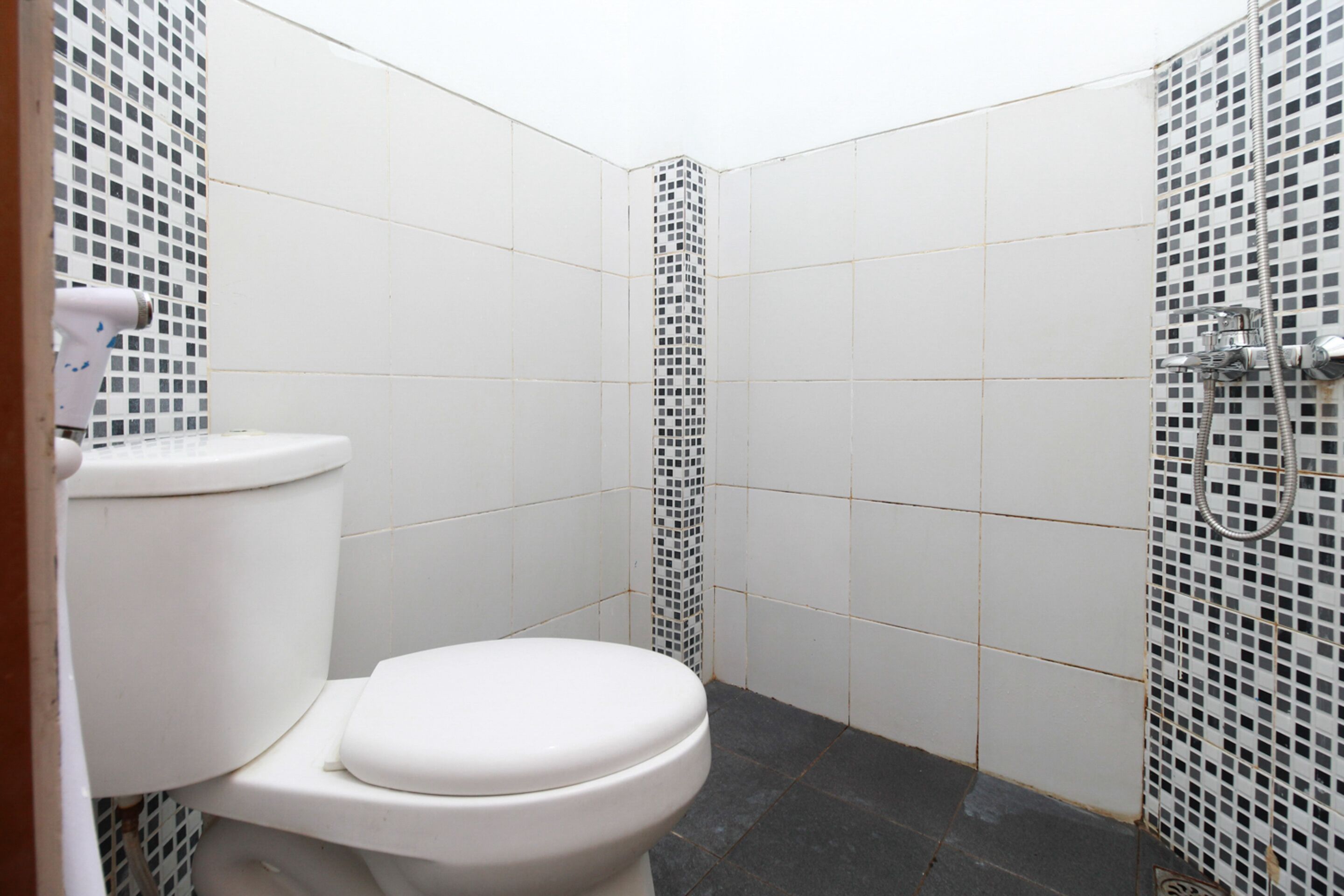 A small, tiled bathroom with a white toilet, a shower area, and a tiled wall.