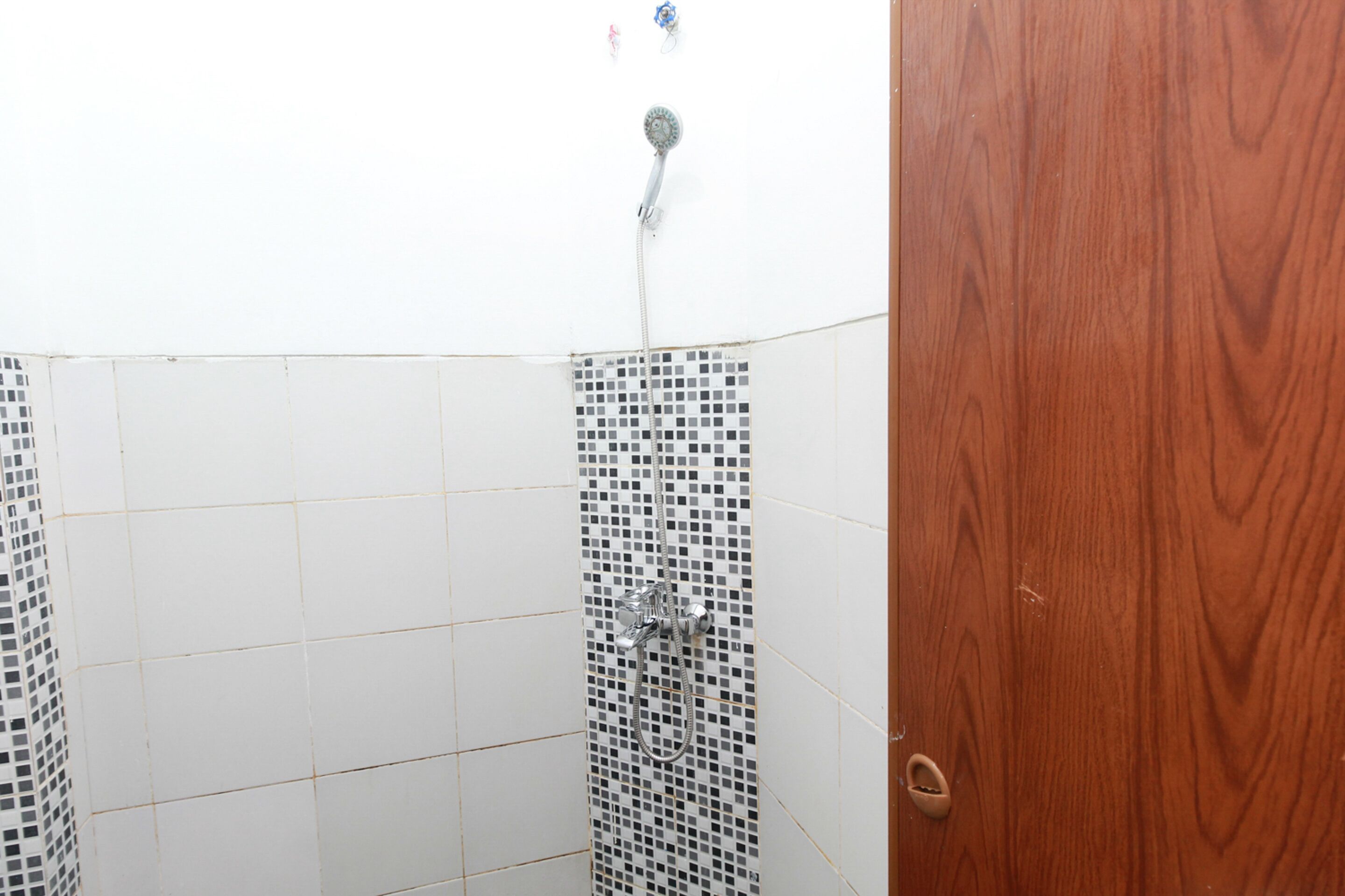 A bathroom with white tiled walls, a shower with a mosaic tile design, and a wooden door.