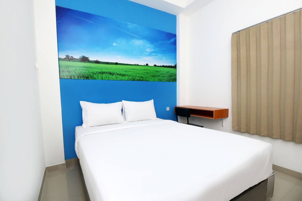 A bedroom with a bed, a nightstand, a wall-mounted shelf, and a window with blinds.