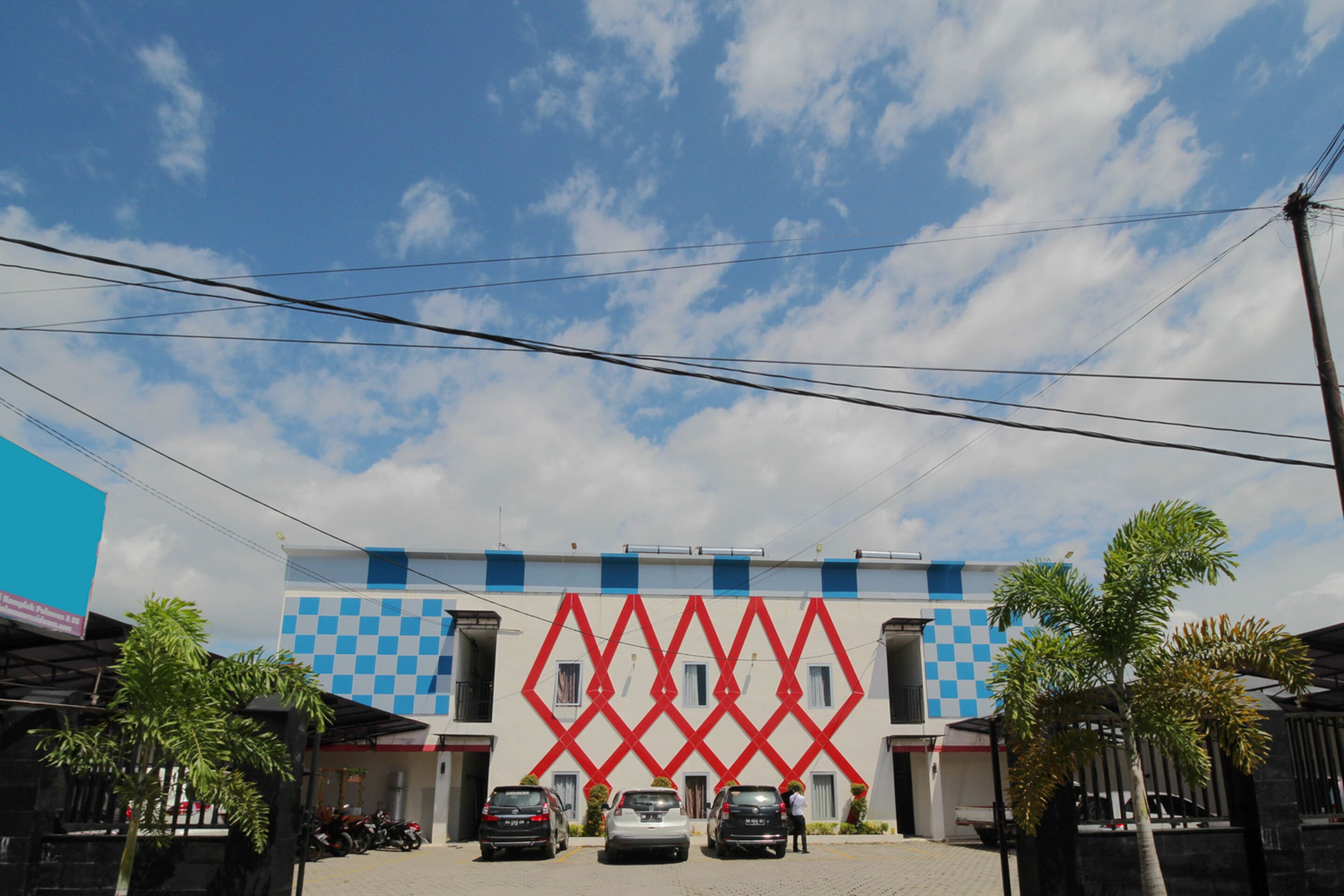 A building with a blue and white facade, a red geometric design, and parked cars in front.