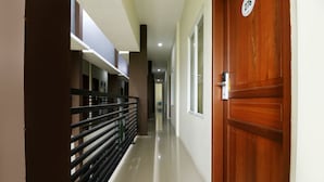Un pasillo con una puerta de madera identificada con el número 276, una barandilla de metal negro y un piso limpio y brillante.