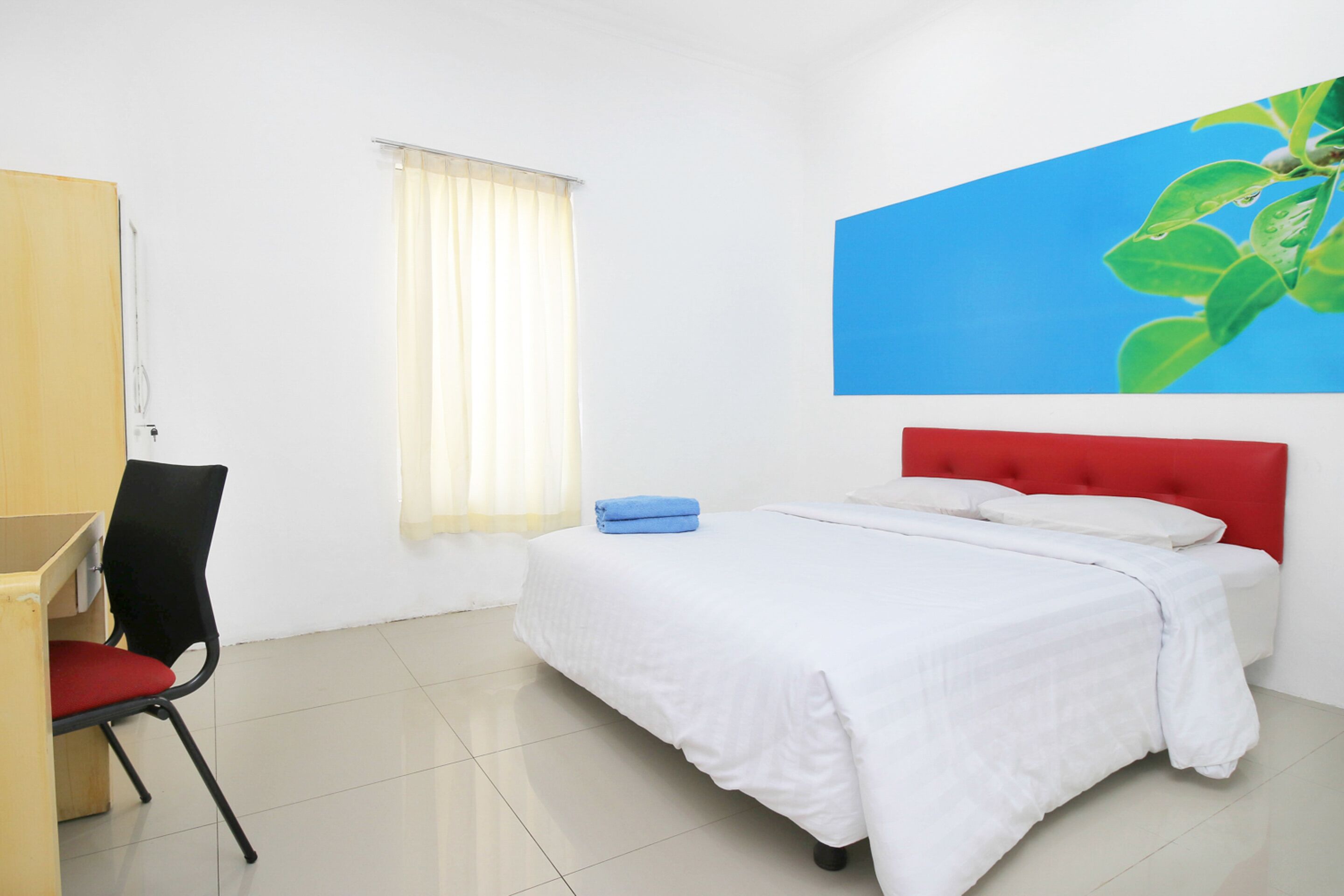 A hotel room with a bed, a desk, a chair, and a window with curtains.