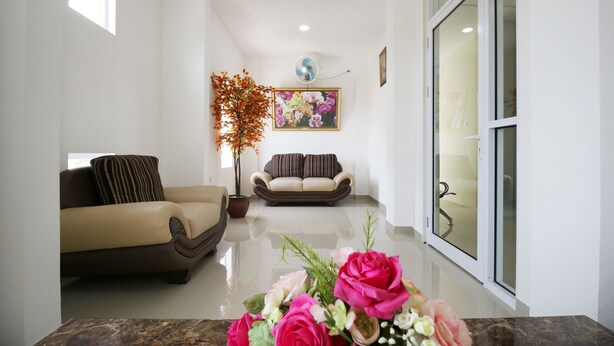 Una sala moderna con un sofá color beige, un sofá marrón, una mesa de centro con un arreglo floral, una planta en maceta y un cuadro en la pared.
