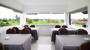 Un salón de conferencias con mesas y sillas, ventanas amplias con vistas a un paisaje verde y edificios.