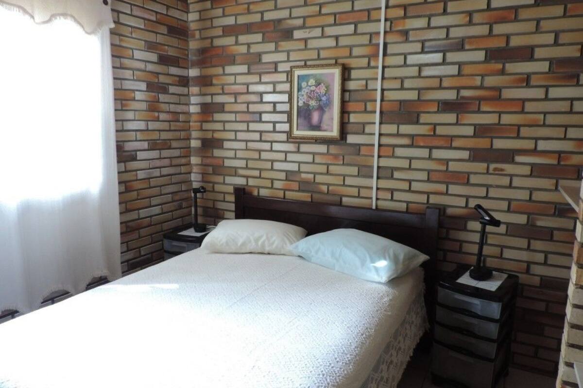 Une chambre avec un mur décoré d’un motif en briques, un lit avec une literie blanche, deux tables de chevet et une petite table de nuit avec une lampe.