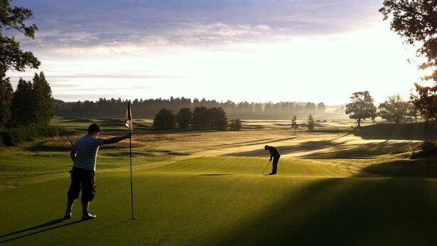 Un terrain de golf avec un mât de drapeau et un golfeur au loin.