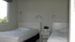 Une chambre double avec deux lits simples, une petite table de chevet agrémentée d’une plante et une fenêtre laissant entrer la lumière naturelle.