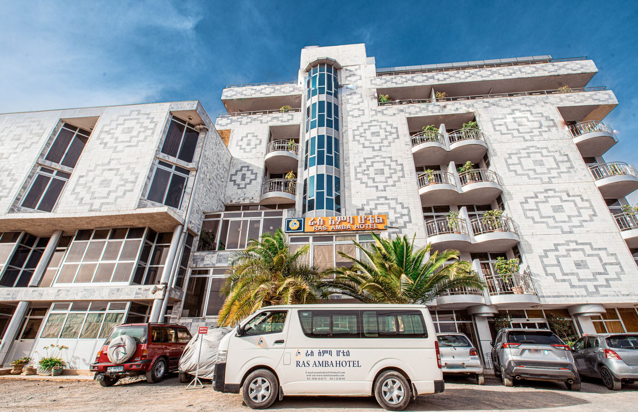 Un edifici de diverses plantes amb façana decorada, balcons i un rètol que anuncia l'Hotel Ras Amba.