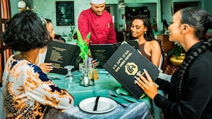 A group of people seated at a table with menus, a chef in a red uniform, and a green tablecloth. - Ras Amba Hotel (Addis Ababa)