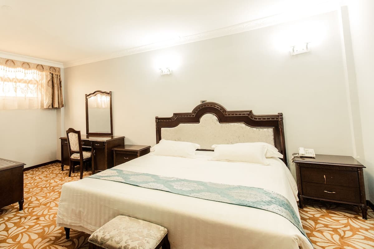 Habitación de hotel con una cama grande, un escritorio con una silla, un espejo y una mesita de noche con un teléfono.