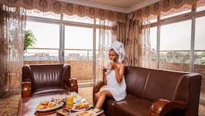 A room with a brown leather sofa, a dining table with breakfast items, and large windows with patterned curtains. - Ras Amba Hotel (Addis Ababa)