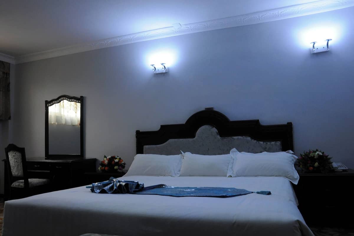 Una cama bien hecha con sábanas blancas, cabecera de madera oscura y dos lámparas fijadas a la pared.