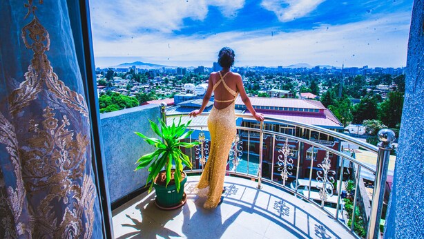 A woman on a balcony overlooking a cityscape with buildings and greenery. - Ras Amba Hotel (Addis Ababa)