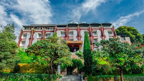 A large, multi-story building with a prominent entrance, surrounded by lush greenery and trees. - Ras Amba Hotel (Addis Ababa)