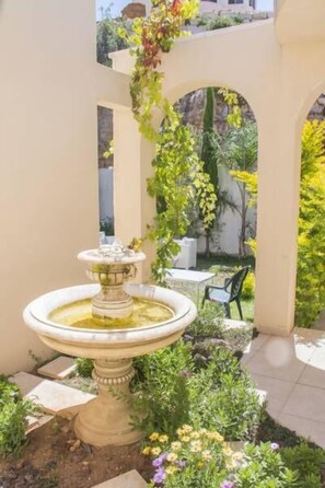 A garden with a fountain, surrounded by plants and a patio area.