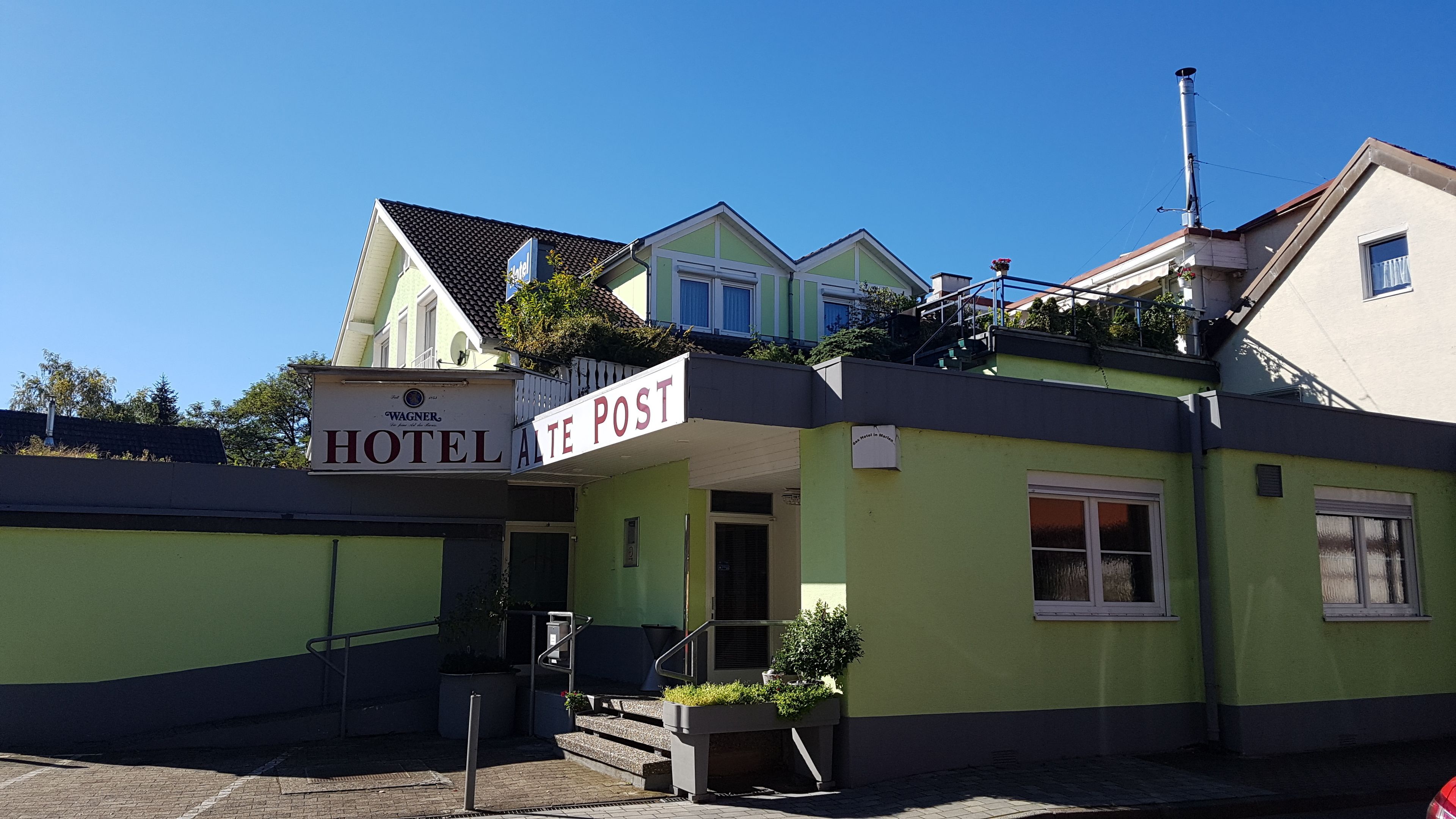 A hotel with a sign reading "Wagner Hotel Alte Post" and a visible entrance with steps leading up to the door.