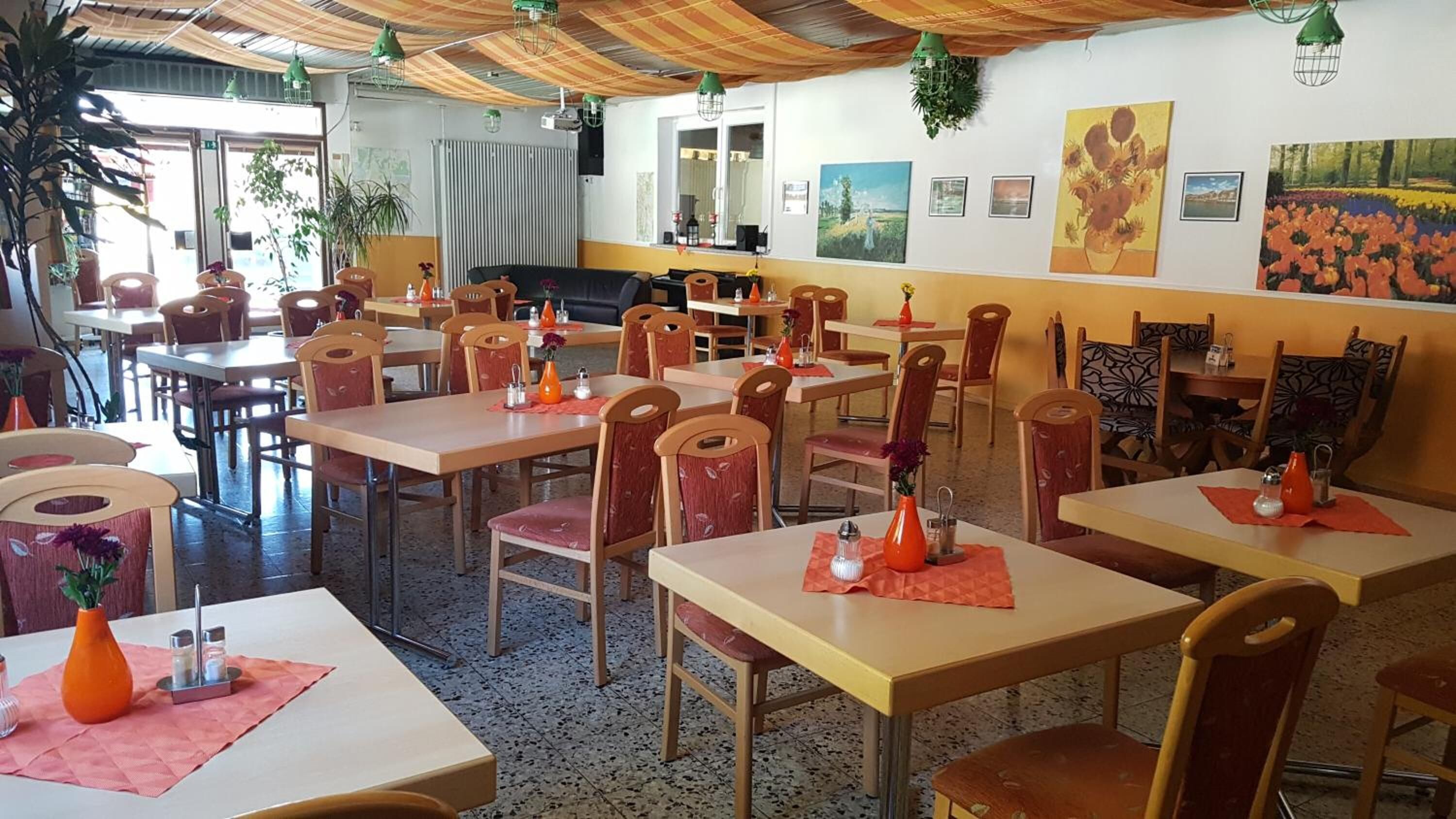 A restaurant with multiple tables and chairs, some with orange napkins and vases.