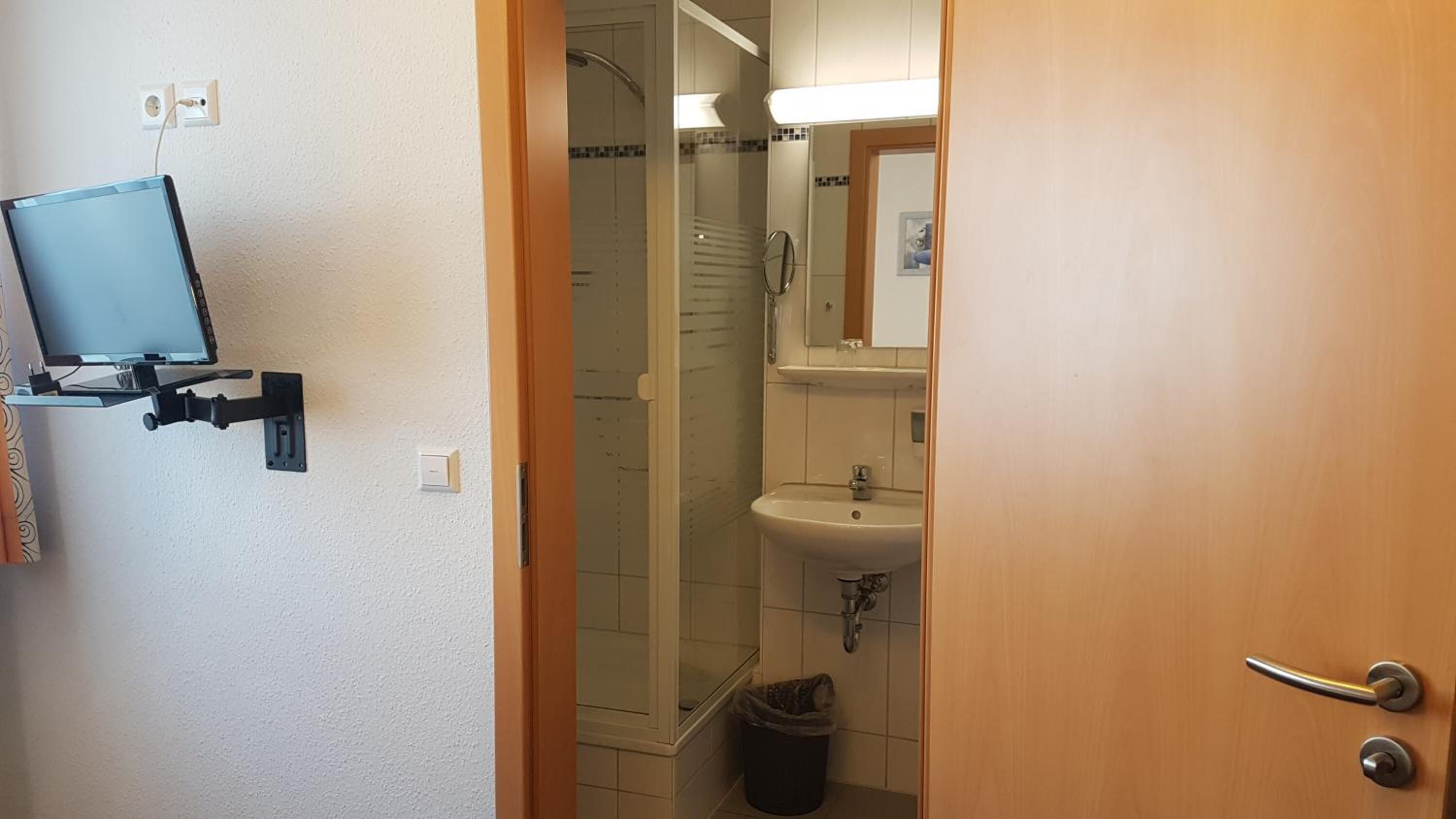 A bathroom with a shower, sink, and a mounted television.