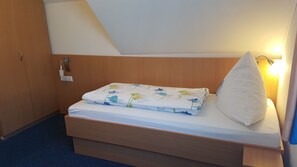 Ein Einzelbett mit blumigem Überwurf, einem weißen Kopfkissen und einer Nachttischlampe.