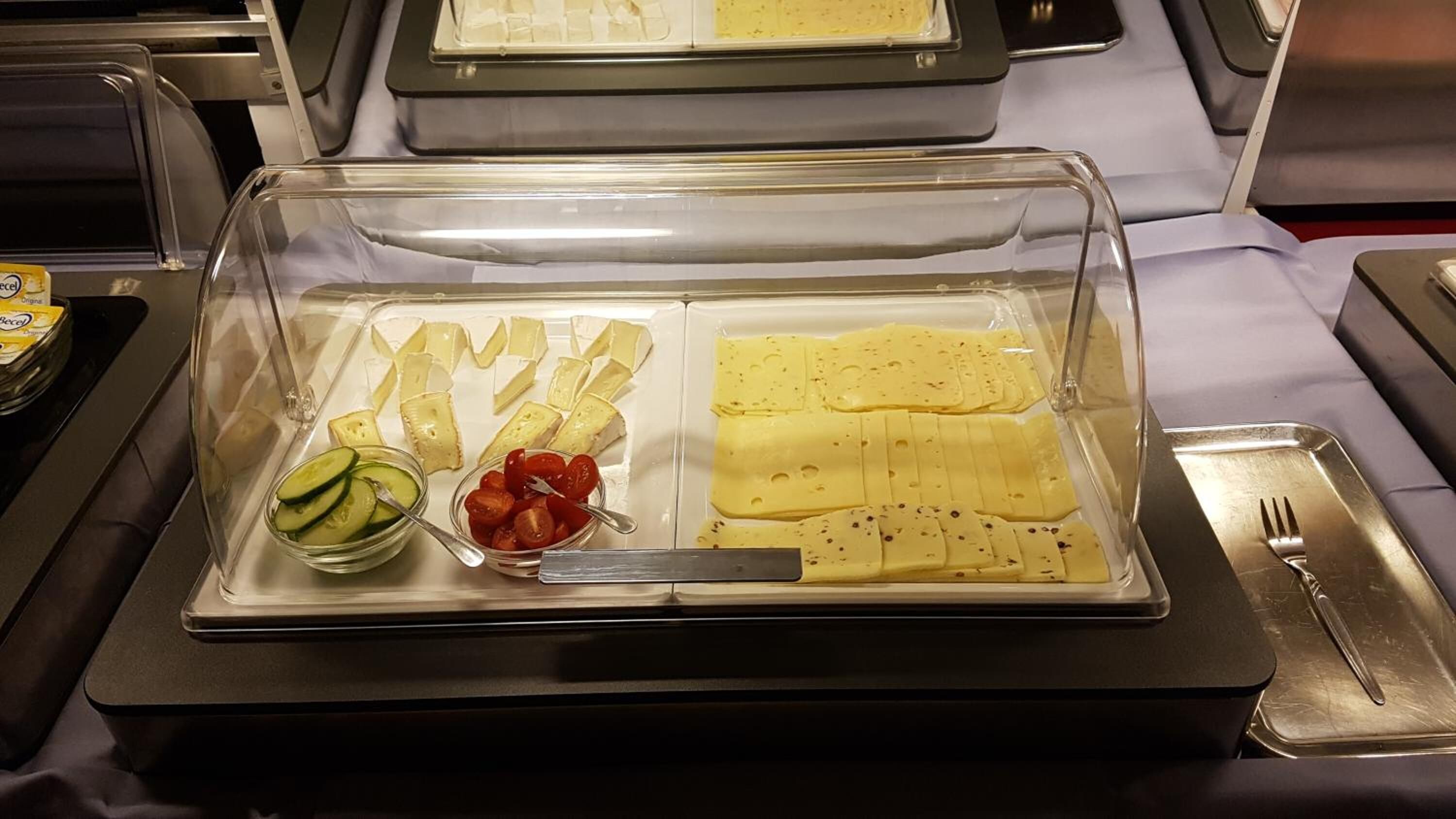 A buffet tray with sliced cheese, cucumbers, cherry tomatoes, and a butter dish.