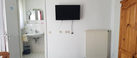 Un baño con lavamanos blanco, espejo y televisor negro montado en la pared.