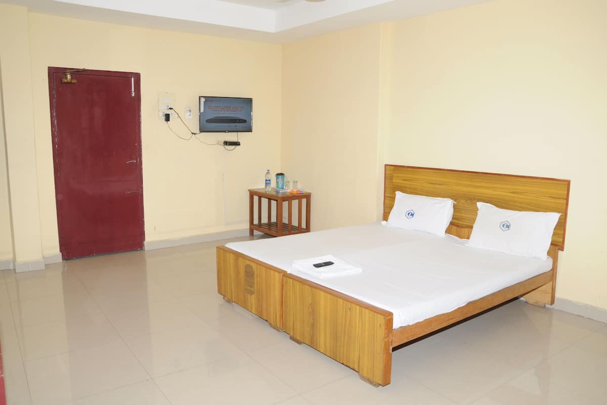 A neatly arranged hotel room with a wooden bed, a red door, a small table with a TV, and a white wall.