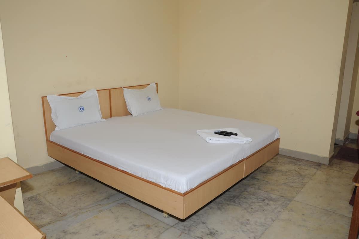 A single bed with a wooden frame, white bedding, and two pillows with a logo. A remote control and a towel are on the bed.