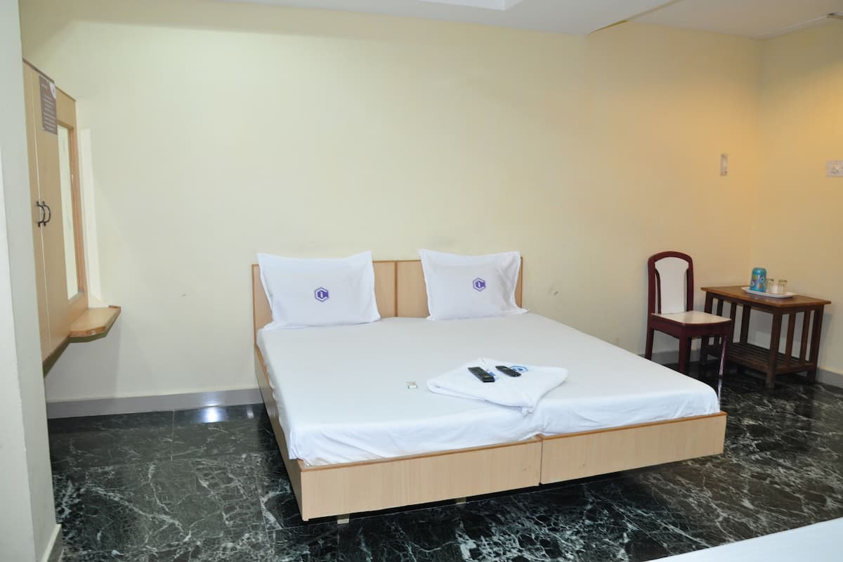 A hotel room with a bed, a wooden nightstand, a chair, and a small table.