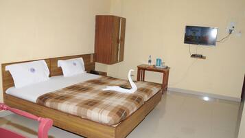 Un dormitorio con una cama de madera, un televisor montado en la pared y una mesita con una botella y una taza.